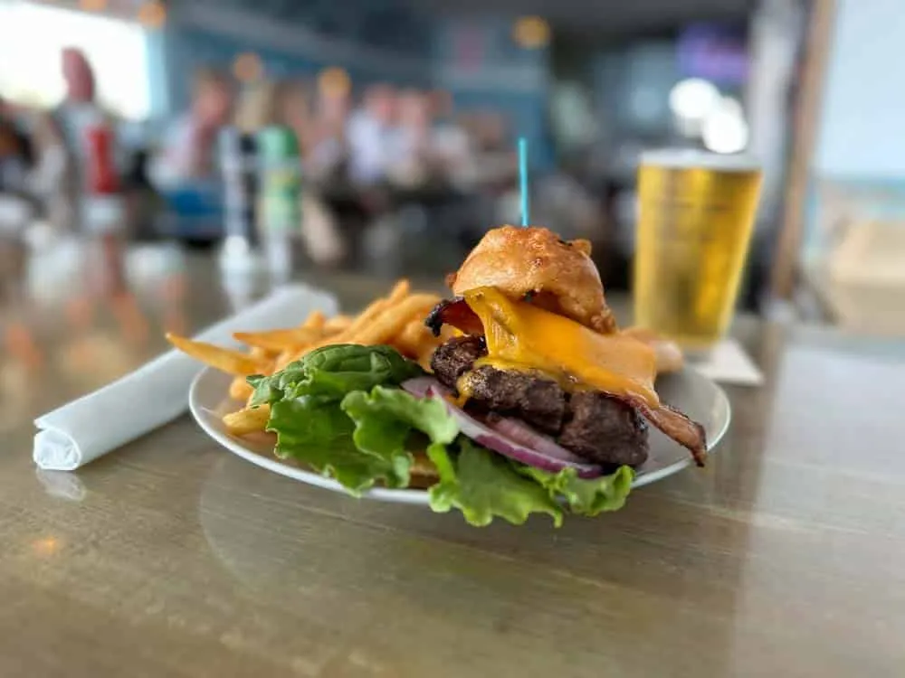 Bacon cheeseburger topped with an onion ring, with fries and a draft beer at the bar
